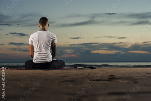 Tattoo man meditating on the beach at sunset