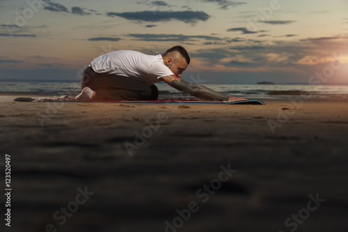 Young man with tattoos practicing yoga on the beach