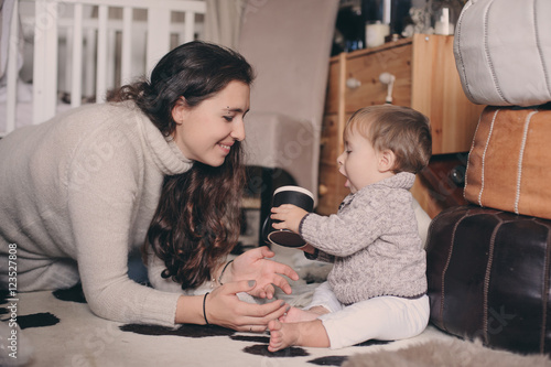 mother and baby son playing together at home. Teaching baby to drink from cup. Happy family lifestyle concept