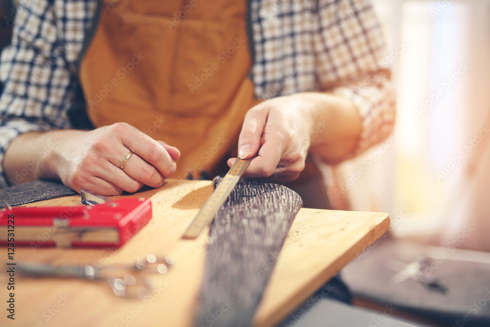 Fototapeta premium Man upholstering chair in his workshop, measure wooden board
