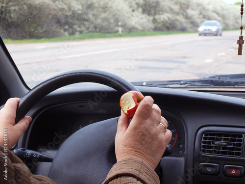 Car driver holding an apple near steering wheel 