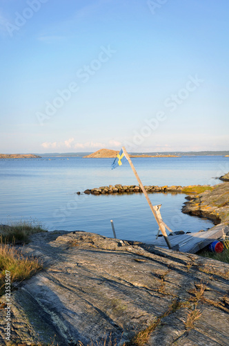 Sommardag på västkusten. En gammal svensk flagga svajar i luften ovanför klipporna. 