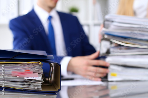 Binders with papers are waiting to be processed with businessman and secretary back in blur. Accounting planning budget, audit, insurance and business concept