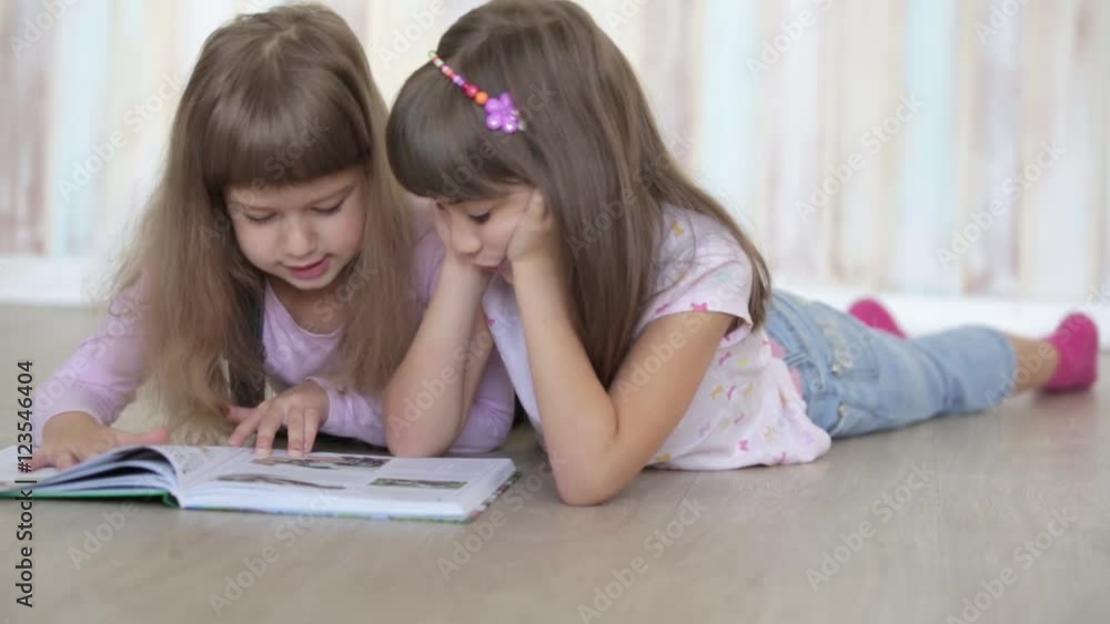two little girls reading a book lying on the floor two little girls reading a book lying on the floor