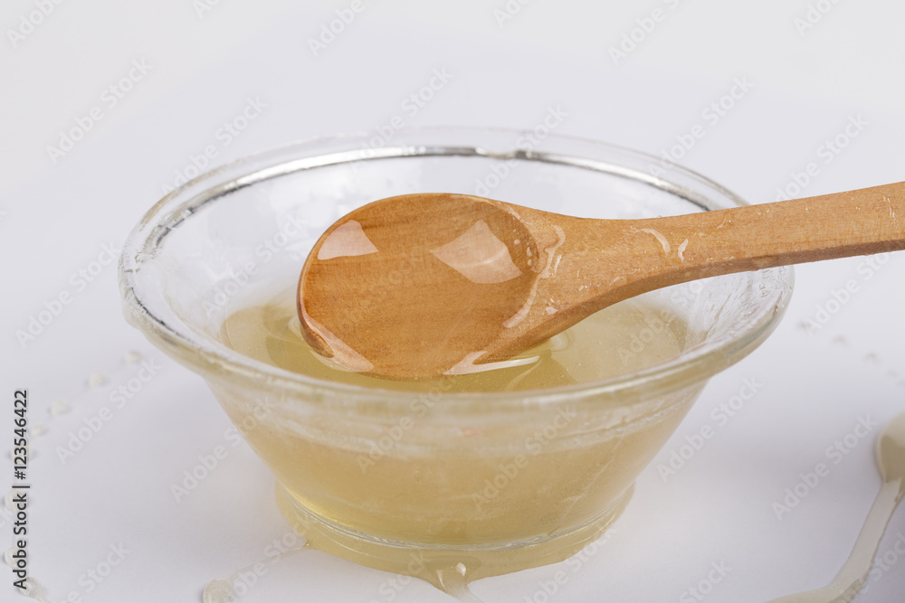 Bee honey in a glass bowl and wooden spoon on white background Bee honey in a glass bowl and wooden spoon on white background