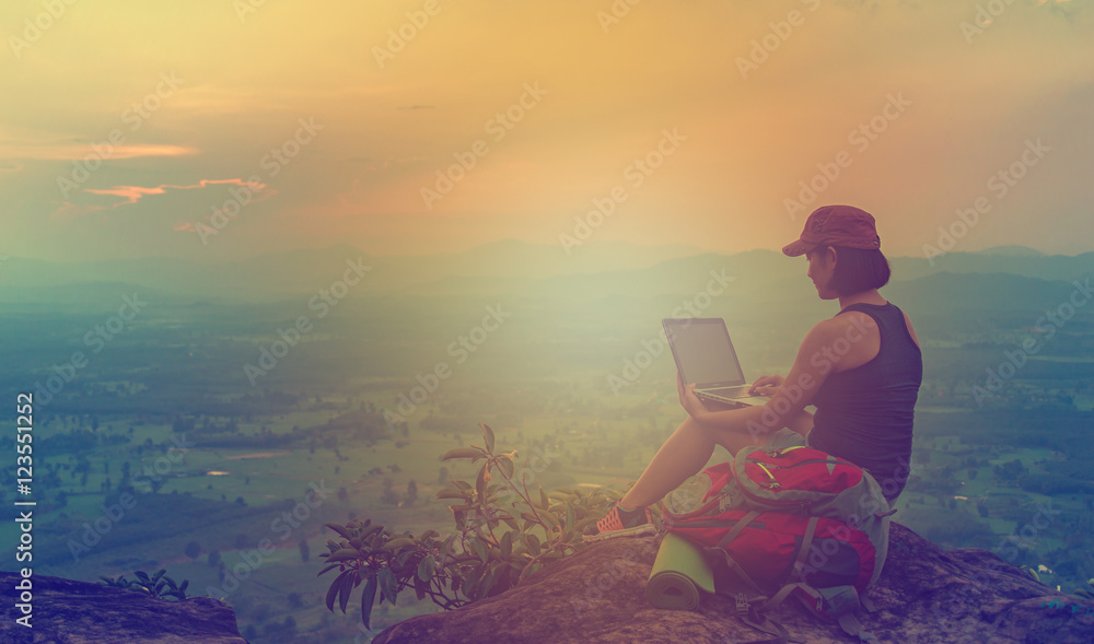 Girls love to dress stylish travelers with a red hat sits on a cliff Computer laptop for e-commerce and cross-process filtering fiery light.