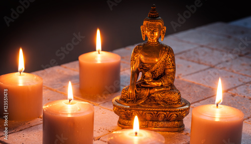 Bronze Buddha with warm lighted candles over limestone background