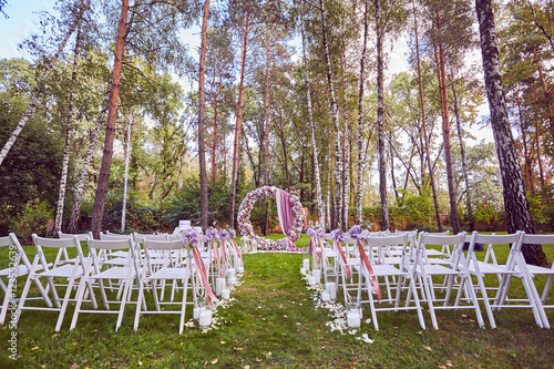 Beautiful wedding set up. Wedding ceremony place in the forest at the evening. White chairs on green grass. photo