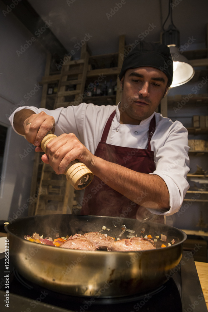 Man pouring pepper on beef cheeks in a pan with sautéed vegetables Man pouring pepper on beef cheeks in a pan with sautéed vegetables