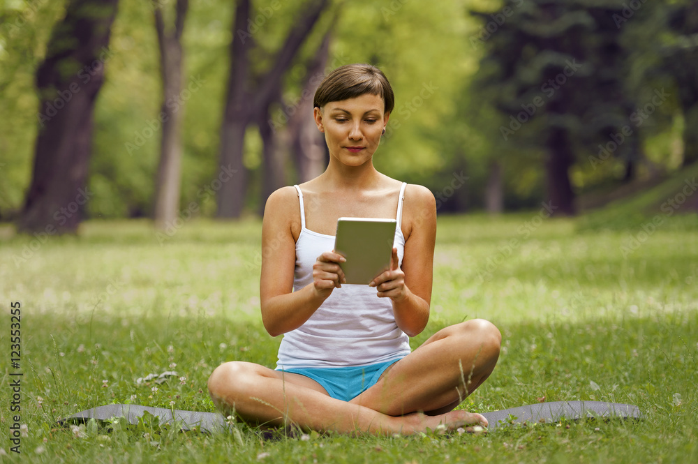 Young woman using tablet outdoor siting on grass, smiling. Young woman using tablet outdoor siting on grass, smiling.