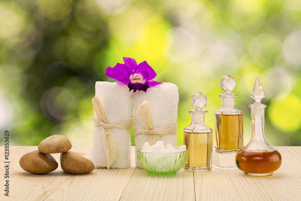 Bottles of aromatic oils with pink orchid, stones and white towel on vintage wooden floor on blurred green bokeh background, spa treatment concept Bottles of aromatic oils with pink orchid, stones and white towel on vintage wooden floor on blurred green bokeh background, spa treatment concept