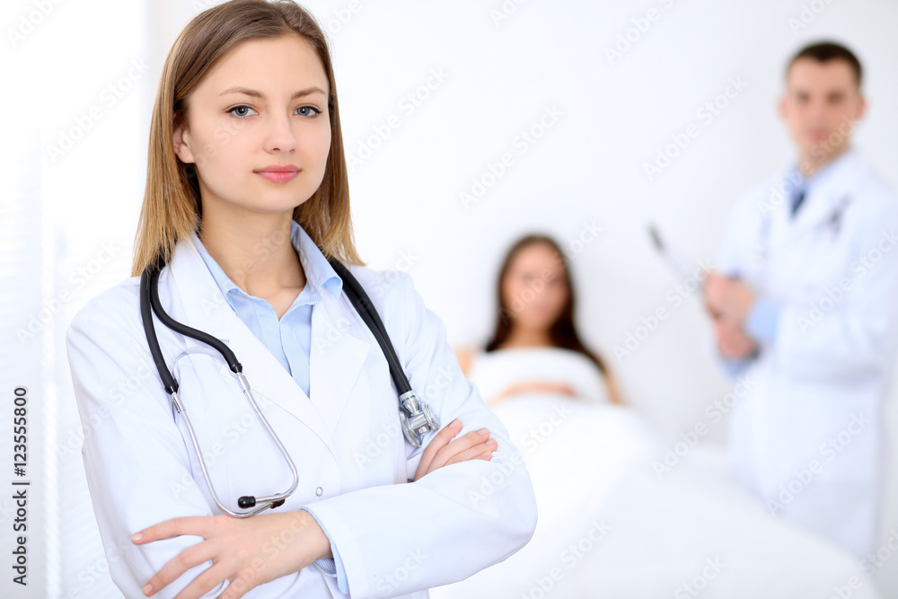 Friendly female doctor on the background with patient in the bed and his physician