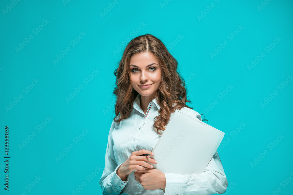 The smiling young business woman with pen and tablet for notes on blue background The smiling young business woman with pen and tablet for notes on blue background