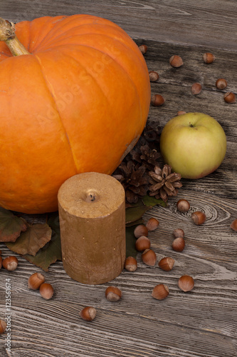 yellow pumpkin, leaves, candle, cone, apple, hazelnut on wooden background