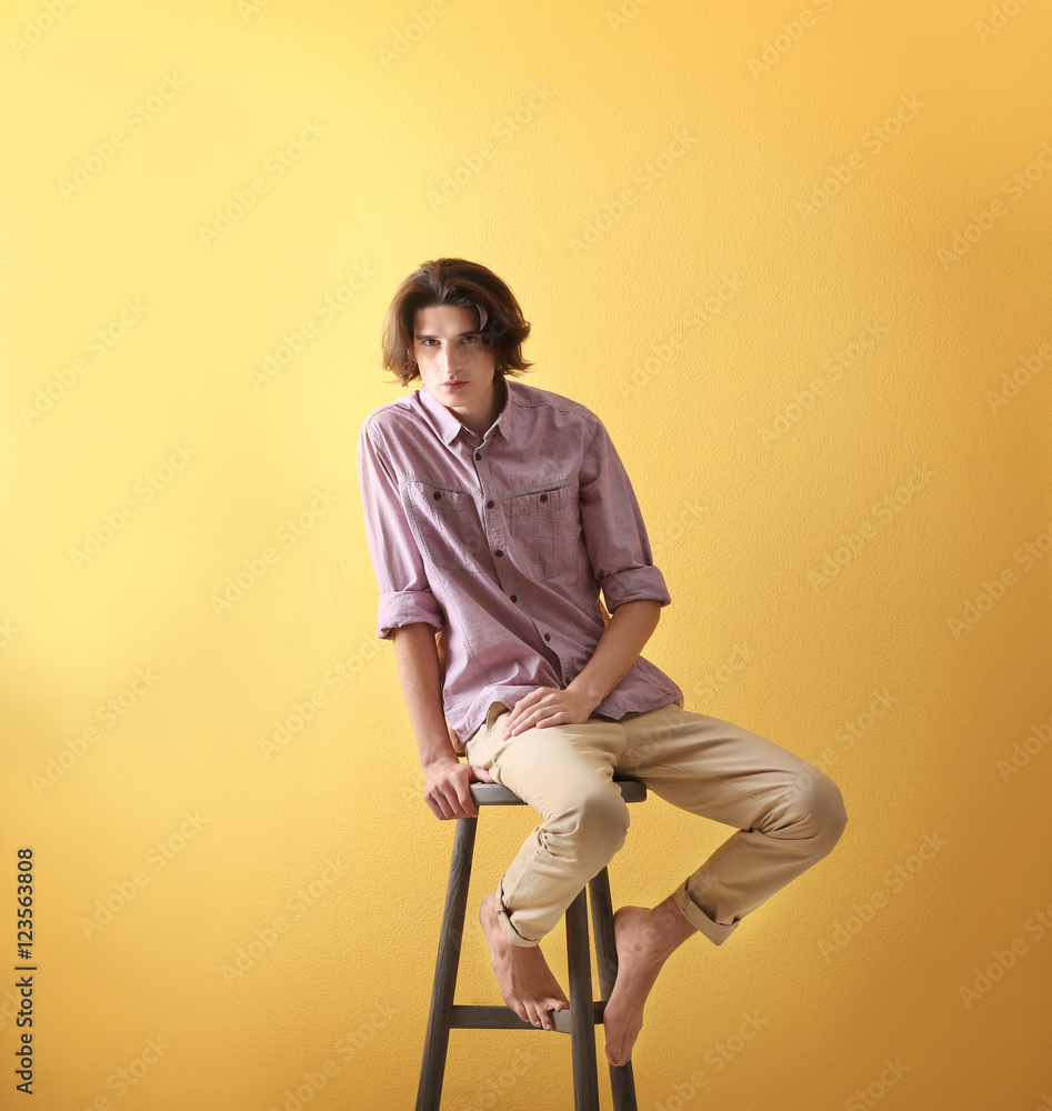 Handsome young man sitting on stool on yellow background Handsome young man sitting on stool on yellow background