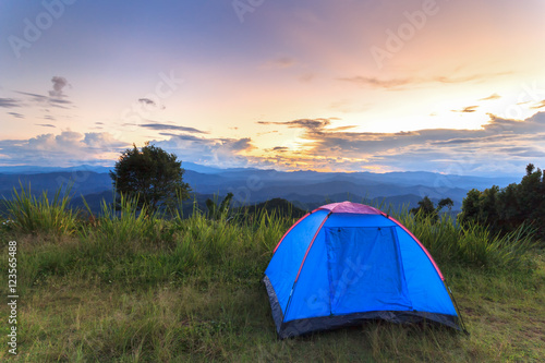 Blue tent standing on grass at top of mountain with sunset 