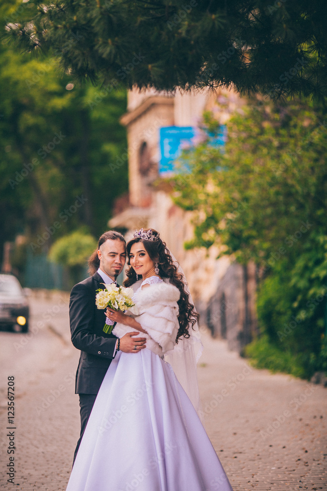 gorgeous wedding couple walking in the old city. Man with long hair and piercing. Woman in beautiful gemstone crystal crown. gorgeous wedding couple walking in the old city. Man with long hair and piercing. Woman in beautiful gemstone crystal crown.