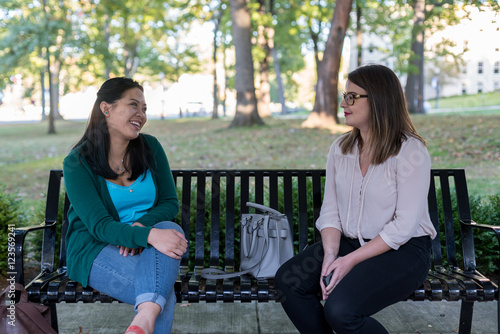 College aged girls sitting on a bench in the park having a conversation