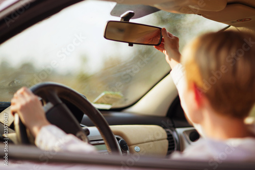 the girl in the car adjusts the rear view mirror