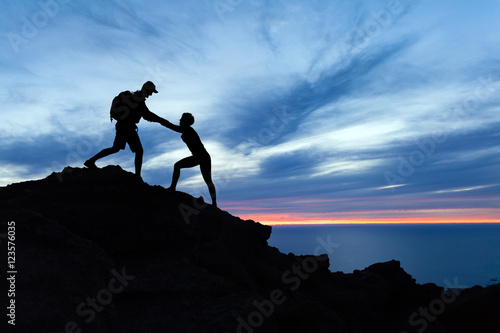 Tableau sur toile Teamwork couple hikers silhouette in mountains, climbers team