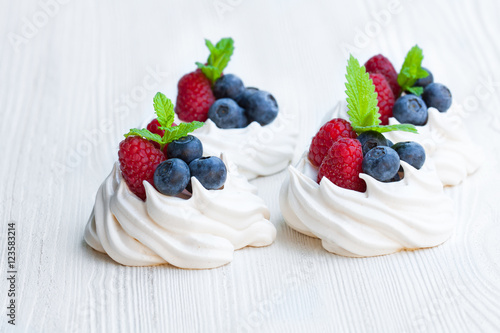 Mini  Pavlova meringue cakes with berries and mint on white wood