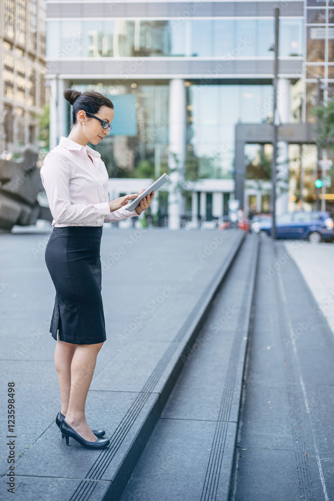 Photo of young attractive businesswoman with modern tablet outdoors, Professional business woman in white shirt and black skirt using modern tablet outdoors, blurred background