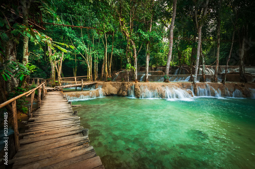 Jangle landscape of tropical rain forest landscape with wooden bridge and amazing turquoise water of Kuang Si cascade waterfall. Luang Prabang, Laos