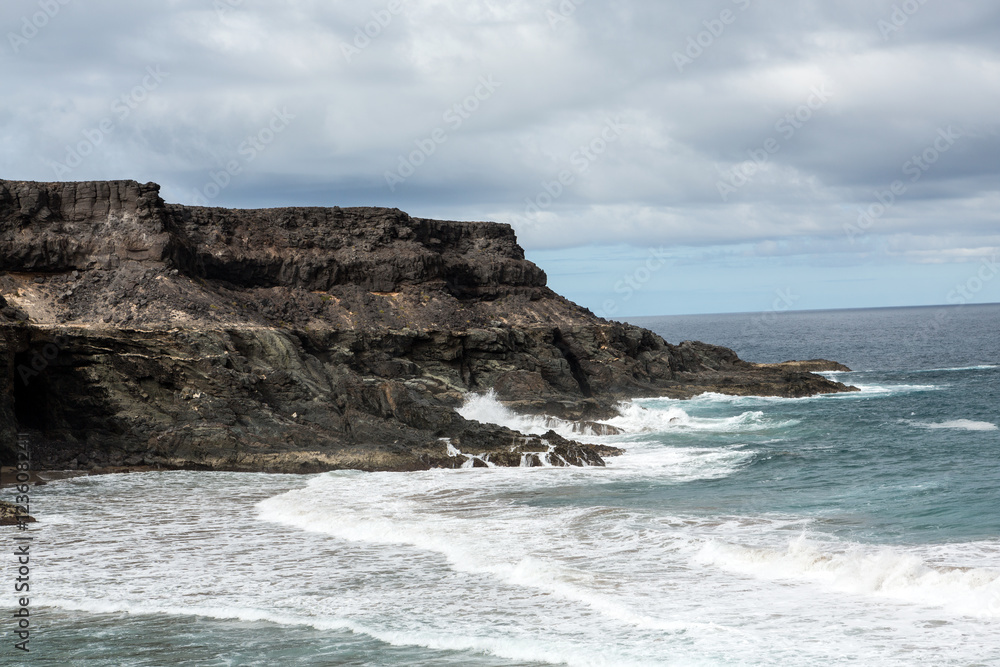 Wave splashing over a rock on the beach of Puertito de los Molinos on Fuerteventura. Canary Island, Spain Wave splashing over a rock on the beach of Puertito de los Molinos on Fuerteventura. Canary Island, Spain