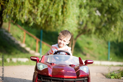 Little cute kid boy driving big red toy in the huge park and enj photo