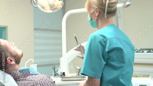 Female dentist examining an drilling patient's tooth. Visit is in proffessional dental clinic. He is sitting on dental chair. He is young and has beard. Dolly and steadicam shot.
 photo