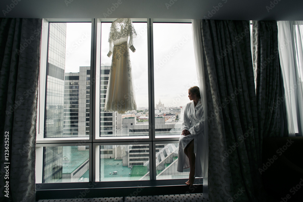 Lady in white bathrobe sits on the windowsill with great industr Lady in white bathrobe sits on the windowsill with great industr