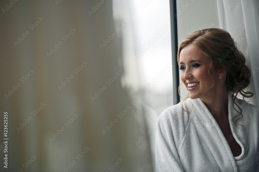 Stunning lady smiles sitting in a bathrobe behind a window