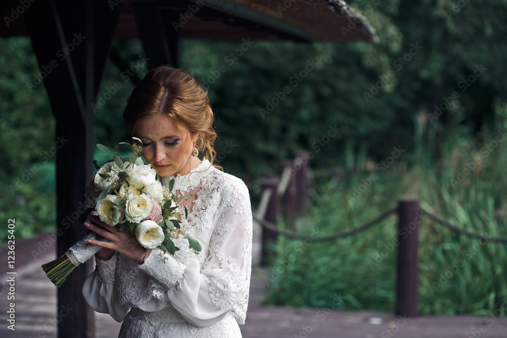 Fototapeta premium Bride stands in the garden holding a wedding bouquet behind her