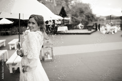 Bride smiles standing in the rain under an umbrella