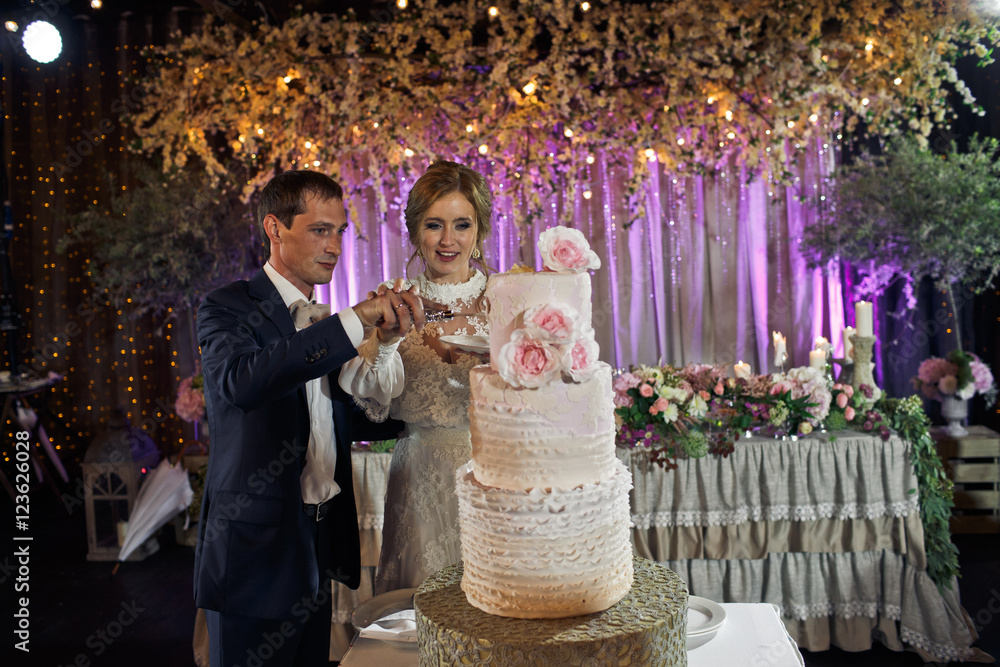 Groom helps bride to cut a wedding cake