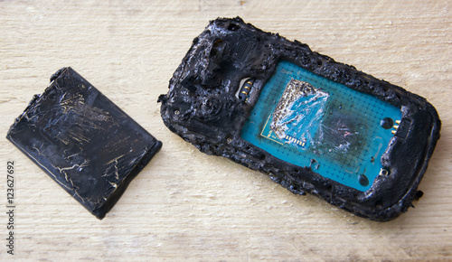 Smartphone with battery problem, mobile phone battery burn due to overheat on wooden background.