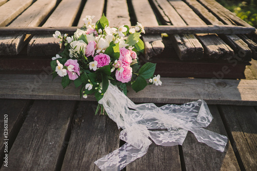 Beautiful bouquet of jasmine and pink garden roses with lace ribbons on old wooden pier
