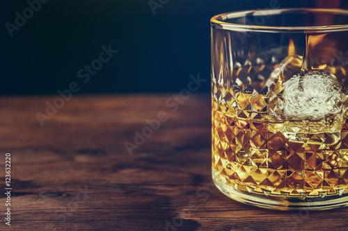 glass of whiskey with ice cubes on wood table, warm atmosphere photo