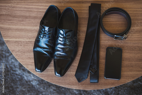 male black shoes, tie, belt and cell phone on wooden table