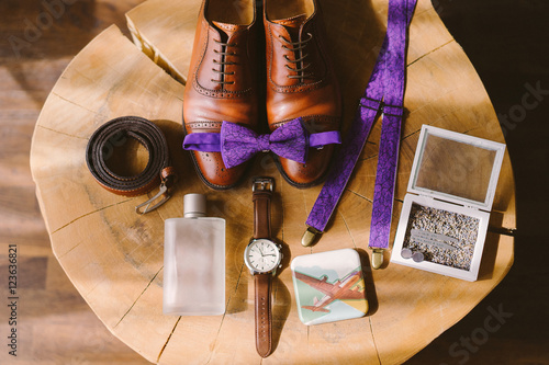 set of groom bow tie, watch, suspenders, belt and perfume lie on the background of vintage wooden table