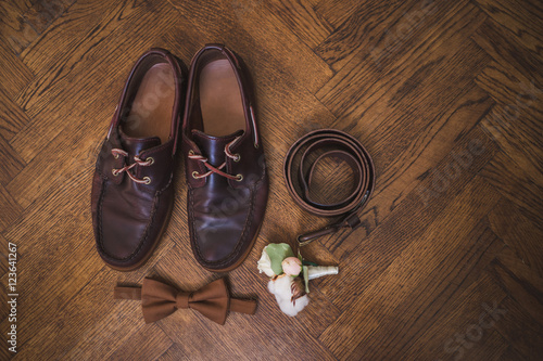 set of groom bow tie, boutonniere, belt and shoes lie on wooden background