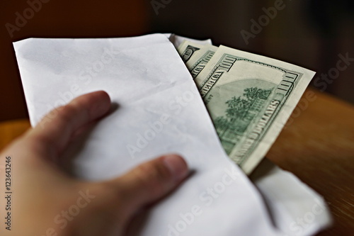 Male hand holding and passing a white envelope full of American Dollars (USD, US Dollars) as a symbol of illegal cash transfer, money laundering or bribery 