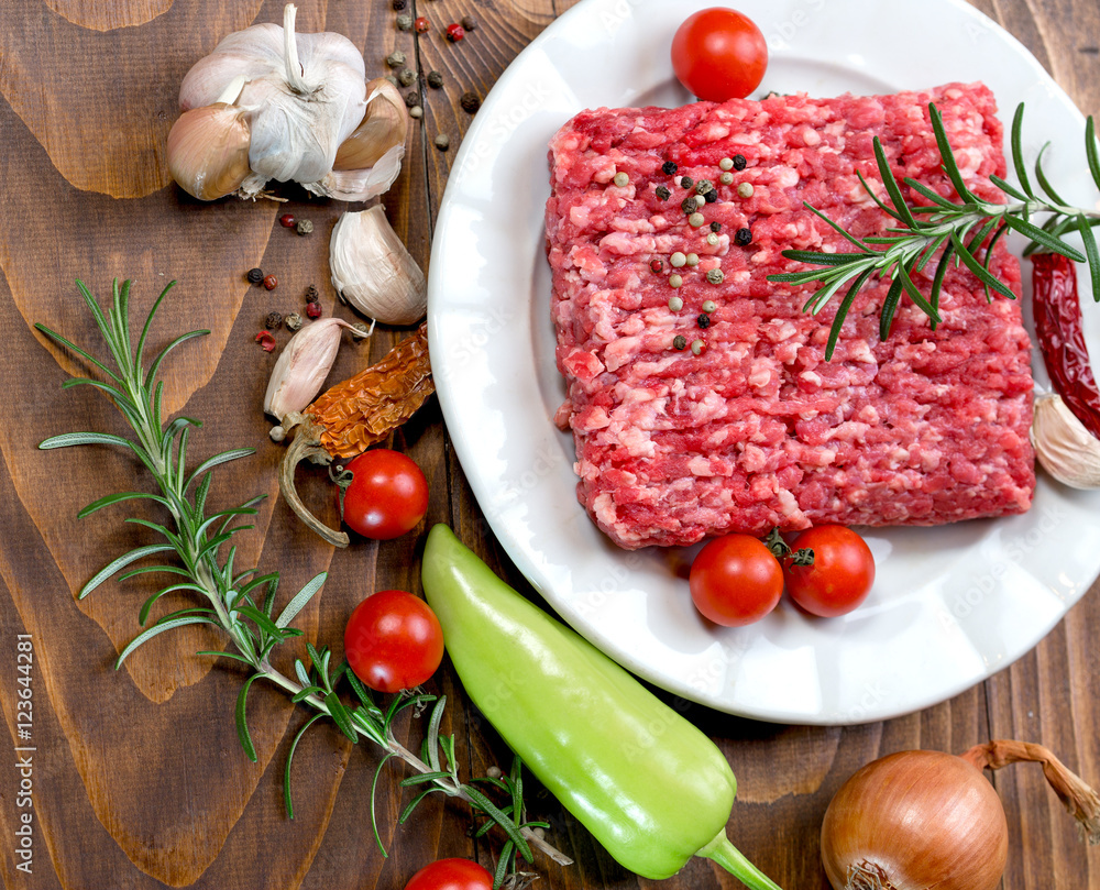 Raw fresh ground beef meat - minced meat on plate and spice (seasoning) with vegetable Raw fresh ground beef meat - minced meat on plate and spice (seasoning) with vegetable