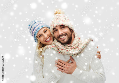 smiling couple in winter clothes hugging over snow