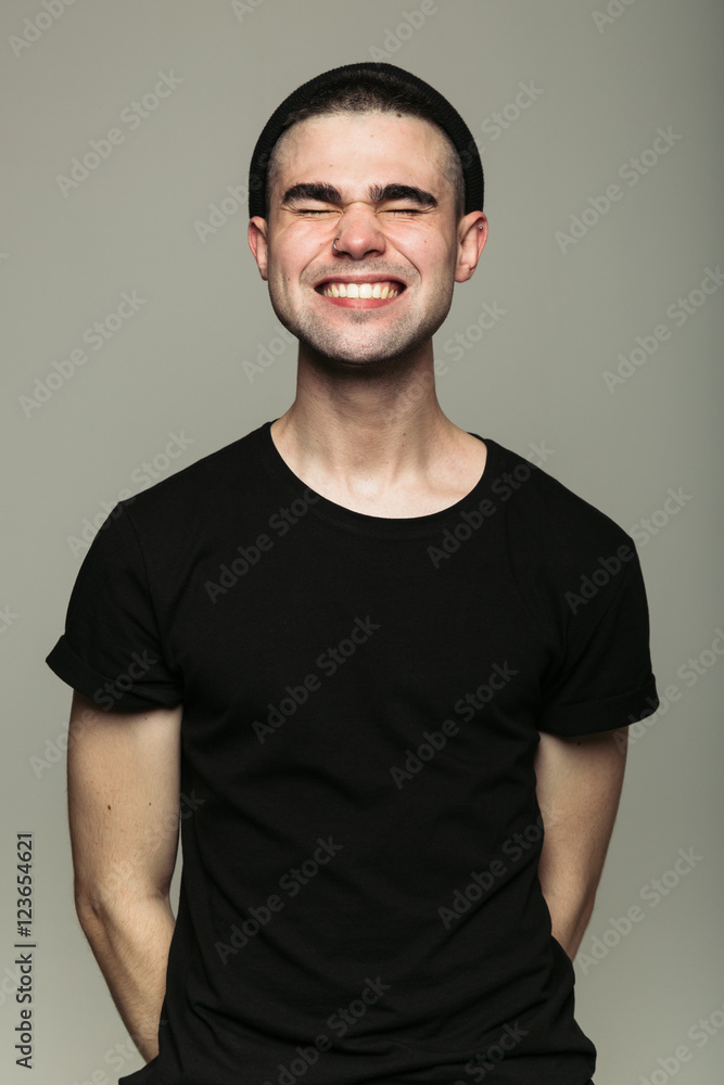 Portrait of young stylish toothy smiling man with closed wink eyes on gray background in studio. Portrait of young stylish toothy smiling man with closed wink eyes on gray background in studio.