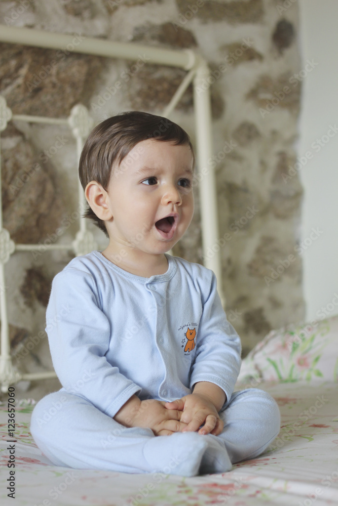 Fototapeta premium shouting baby sitting in bed with stone background