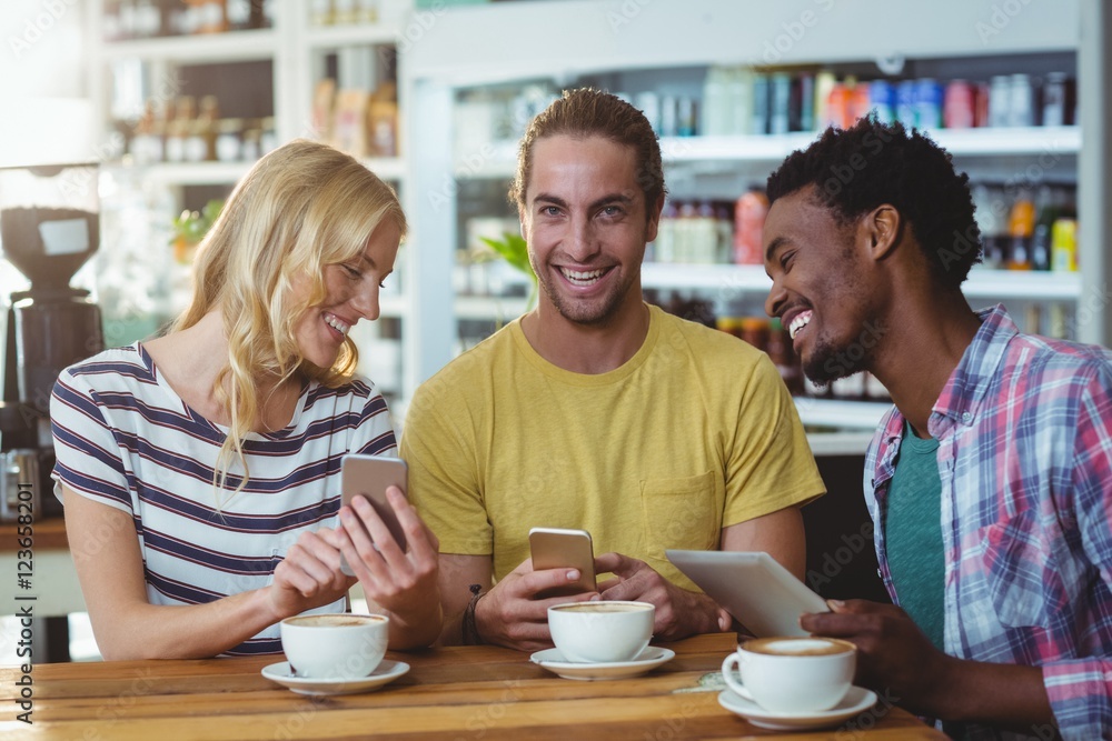 Three friends using mobile phones while having cup of coffee Three friends using mobile phones while having cup of coffee