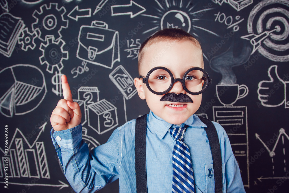 Little boy as businessman or teacher with mustache and glasses standing on dark background pattern. Wearing shirt, tie. Lifting a finger up Little boy as businessman or teacher with mustache and glasses standing on dark background pattern. Wearing shirt, tie. Lifting a finger up