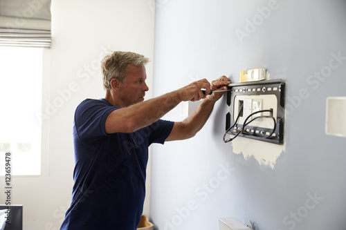 Man Fitting Bracket For Flat Screen TV Onto Wall