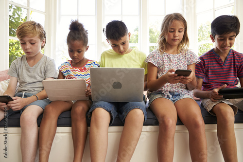 Group Of Children Sit On Window Seat And Use Technology